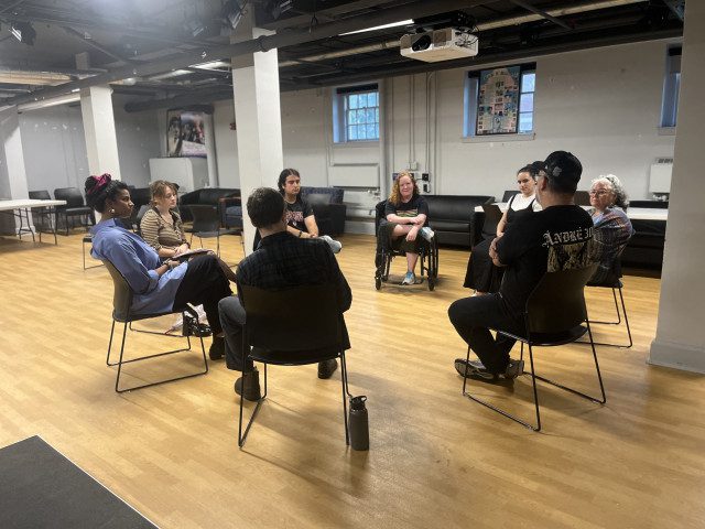 Theater class sits in a circle in a blackbox theater